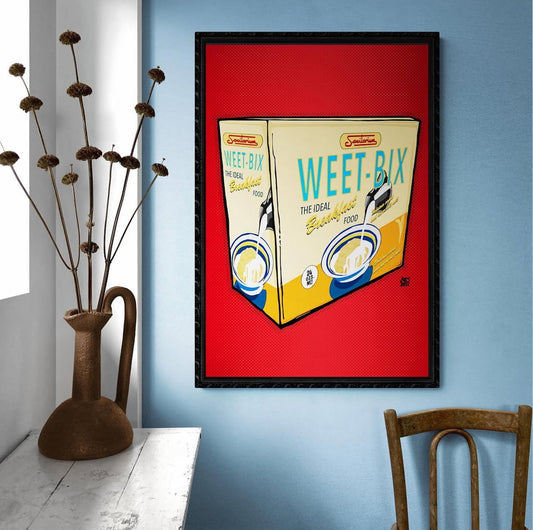 Framed artwork of a Weet-Bix cereal box on a blue wall with a vase and chair in the foreground.