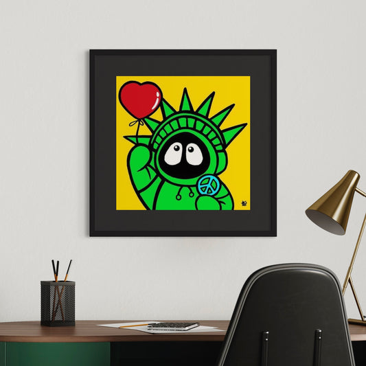 Framed colorful artwork of Hoodie Boy resembling the Statue of Liberty holding a heart and peace symbol on a yellow background, displayed in an office setting.