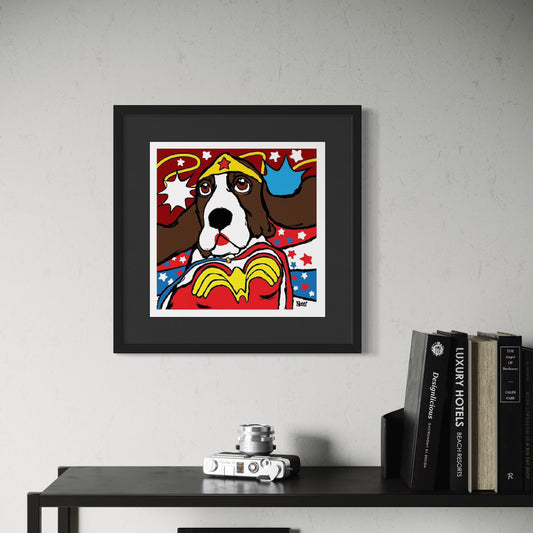 Framed artwork of a Basset Hound dressed as Wonder Woman on a wall above a table with books and a camera.