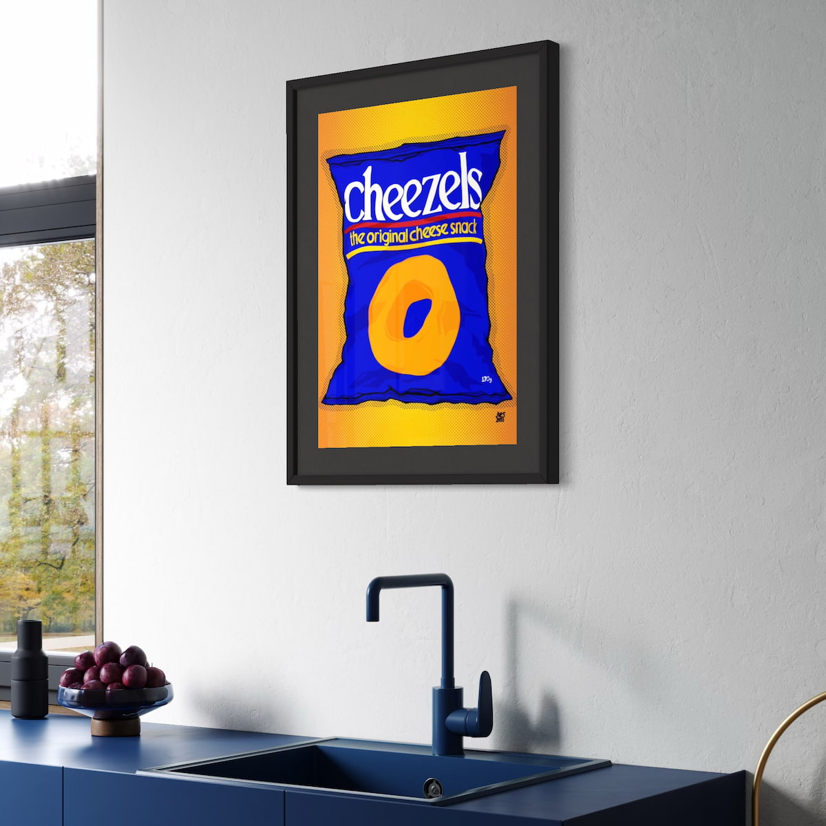 Framed Cheezels snack packet art on a kitchen wall above a sink.