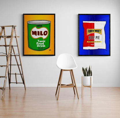 Two framed artworks of Australian iconic food packaging on a wall with a chair and plant in the foreground.