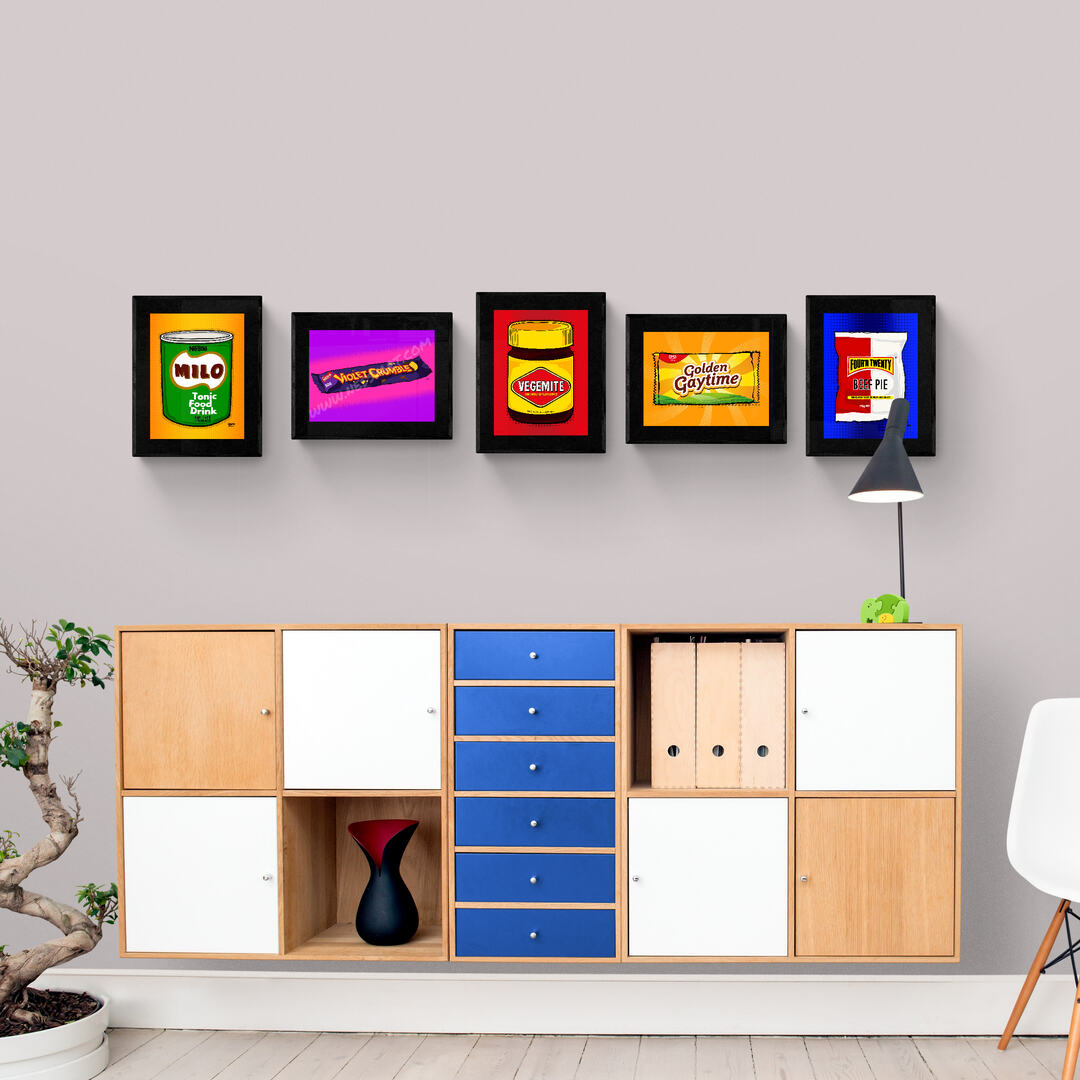 Framed colorful vintage food packaging art on a wall above a wooden cabinet.
