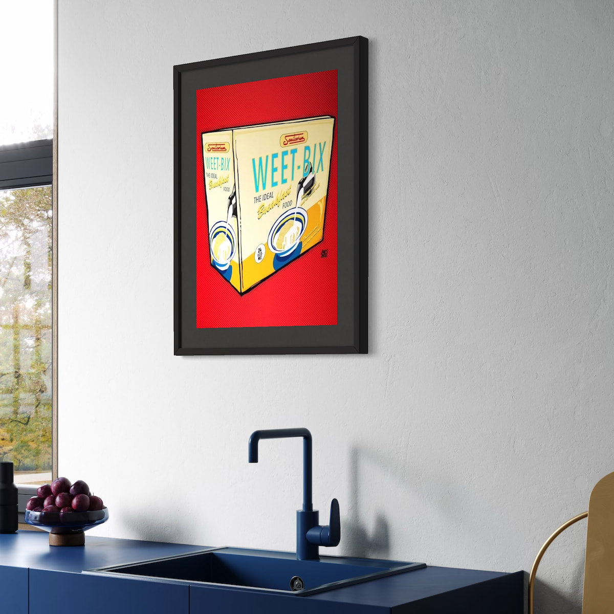 Framed artwork of a Weet-Bix cereal box on a kitchen wall above a sink.