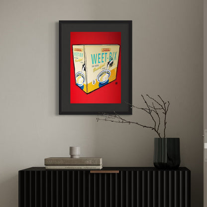 Framed artwork of a Weet-Bix cereal box on a wall above a black console table.