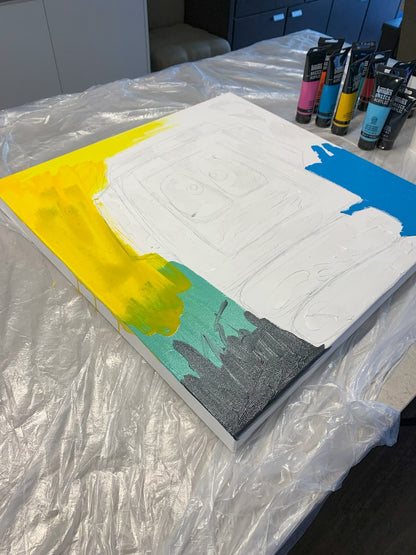 Artistic abstract painting on a canvas with various colors on a plastic-covered table.