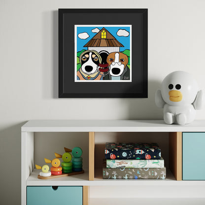 Two dogs in front of triangular-roofed house—playful cartoon homage to American Gothic with expressive faces, blue sky, and yellow window. Staged above white cabinet with stacking toys, patterned boxes, and bird-like figurine. Giclée print, 18x18cm from Nessy Pop Art