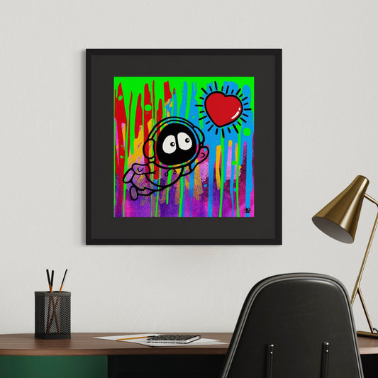 Framed colorful artwork with Hoodie Boy floating towards a shining heart with a colorful dripping background, on a wall above a desk with office supplies.
