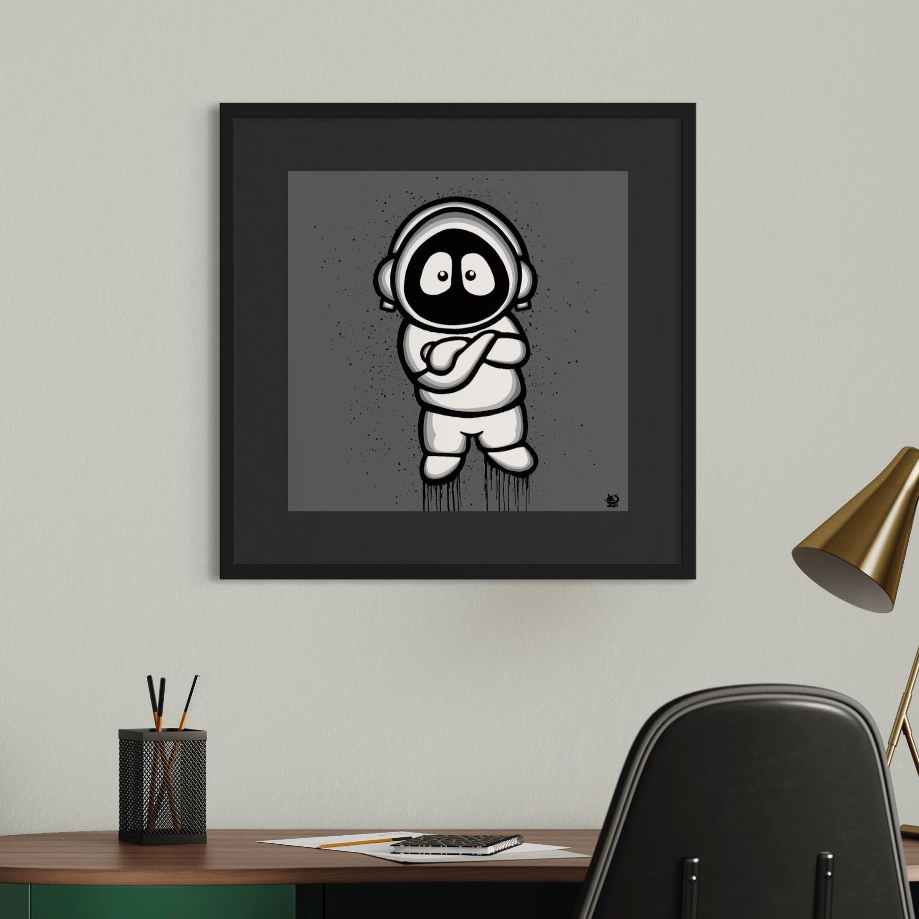 Framed black and white illustration of Hoodie Boy, arms folded, with a gray background, on a white wall above a desk.