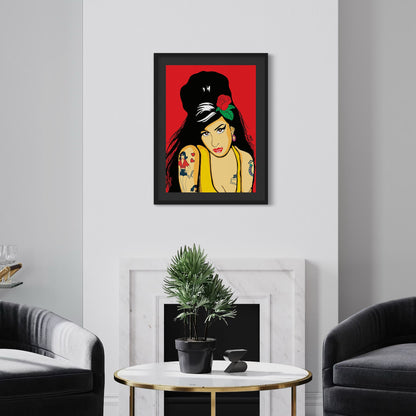 Framed artwork of a Amy Winehouse on a wall above a round table with a plant.