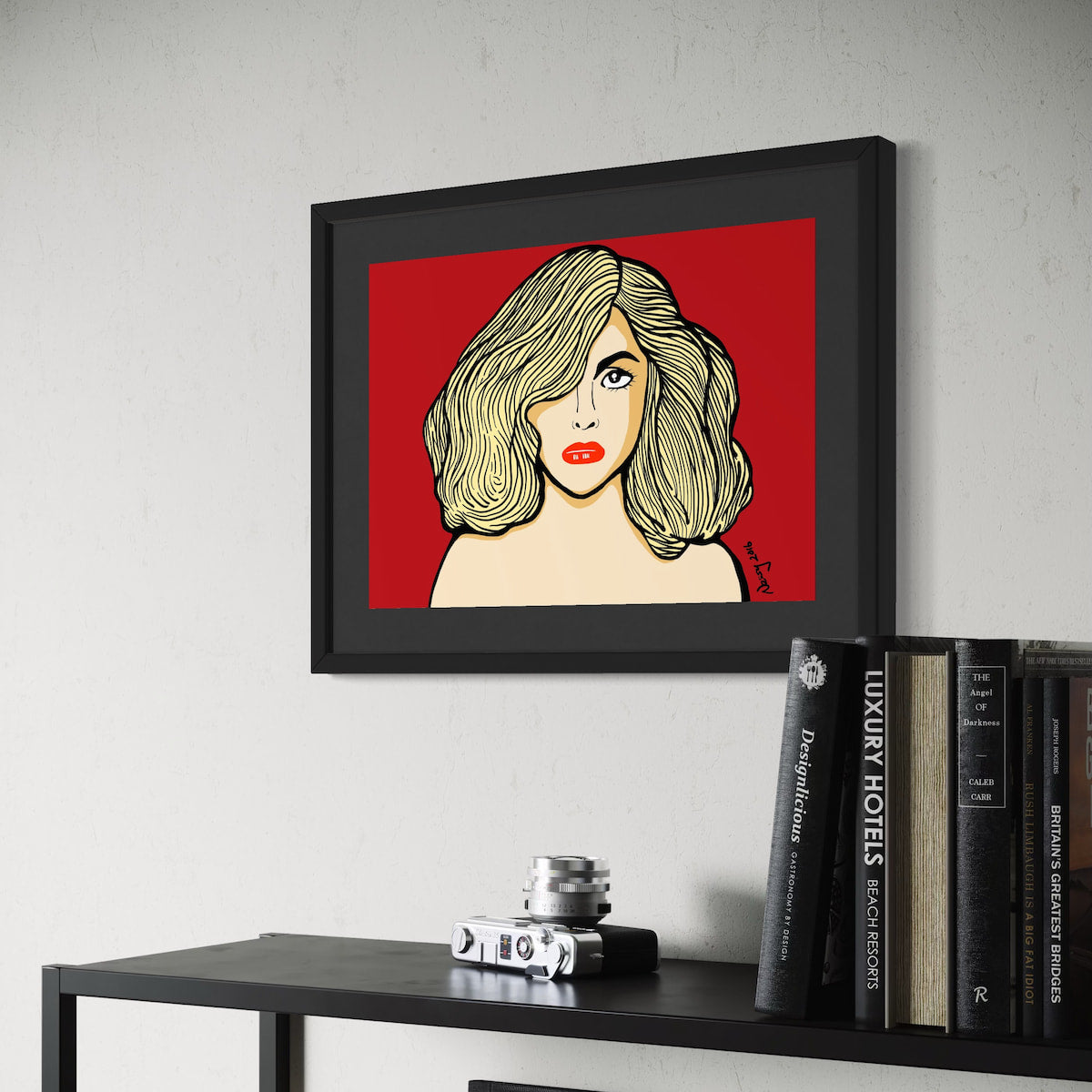 Gaga in red—blonde waves, bold lashes, and lips that dare. A3 giclée from Nessy Pop Art, framed above a shelf of travel books and vintage camera. A pop icon rendered in pure attitude.