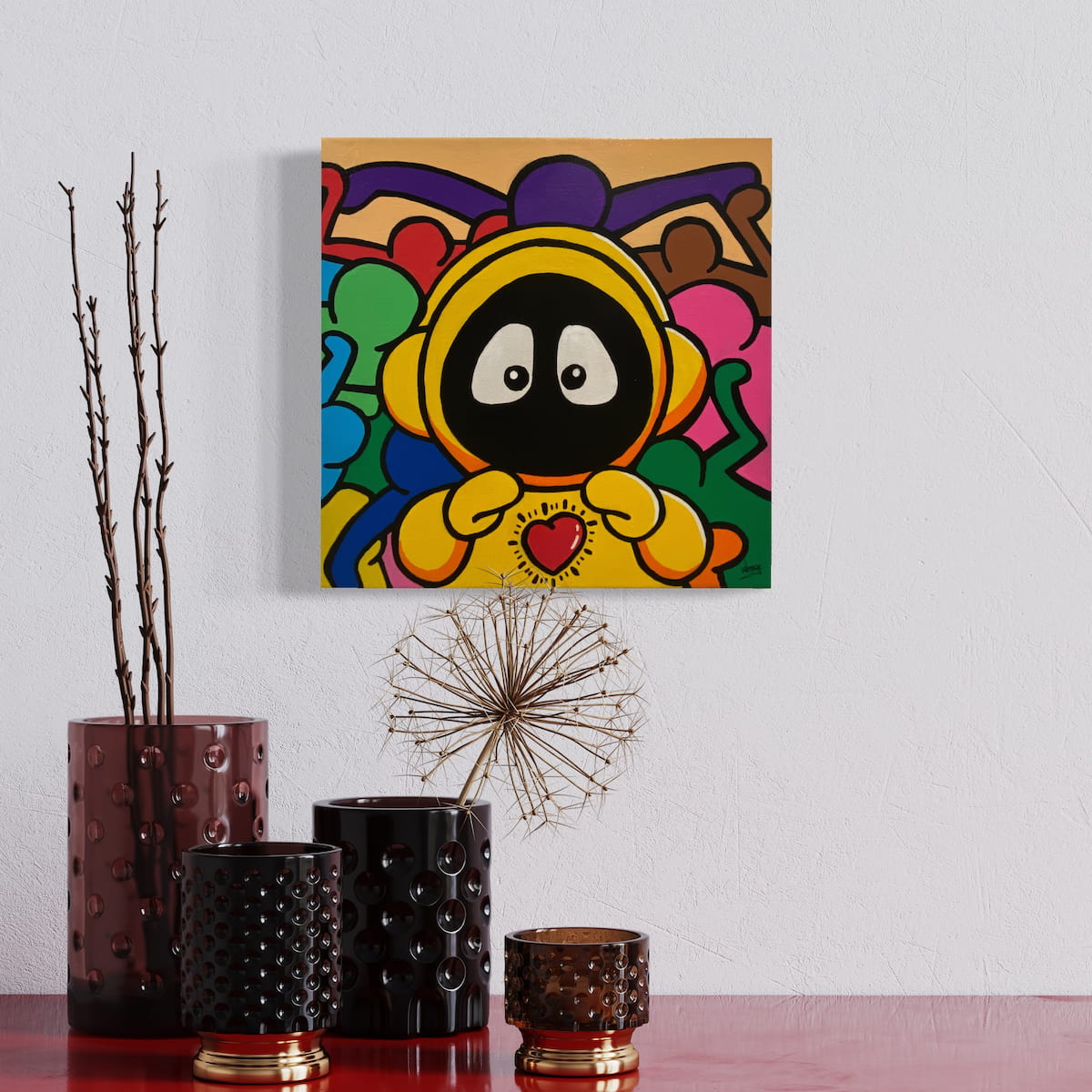 Colorful painting of Hoodie Boy in yellow with a heart on his chest and Keith Haring characters surrounding him, on a wall above decorative vases.