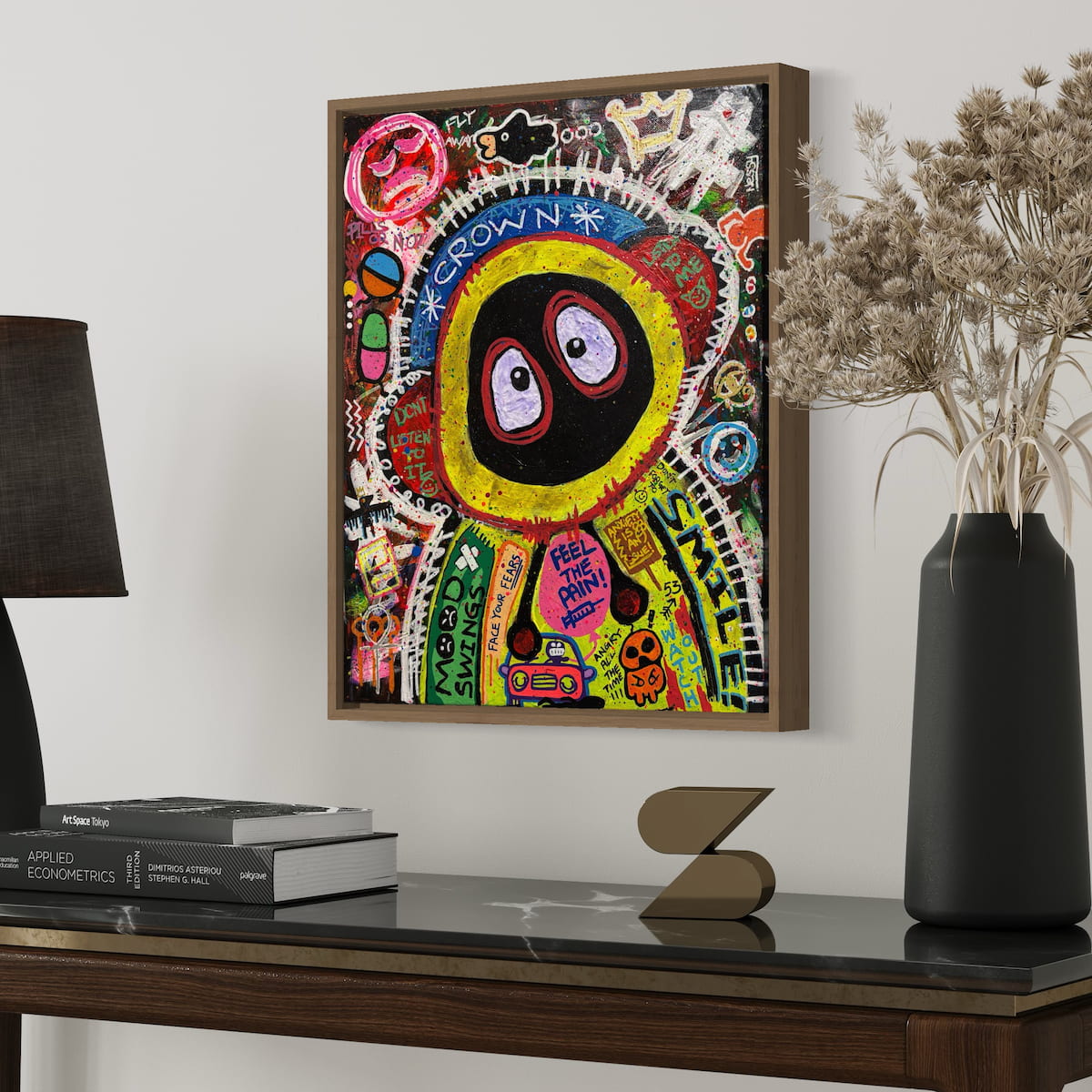 Colorful painting of Hoodie Boy in a Basquait style in a wooden frame on a wall above a desk with decor items.