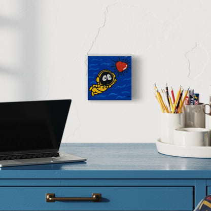 Laptop on a blue desk with a small painting of Hoodie Boy swimming towards a shinning heart, above it.