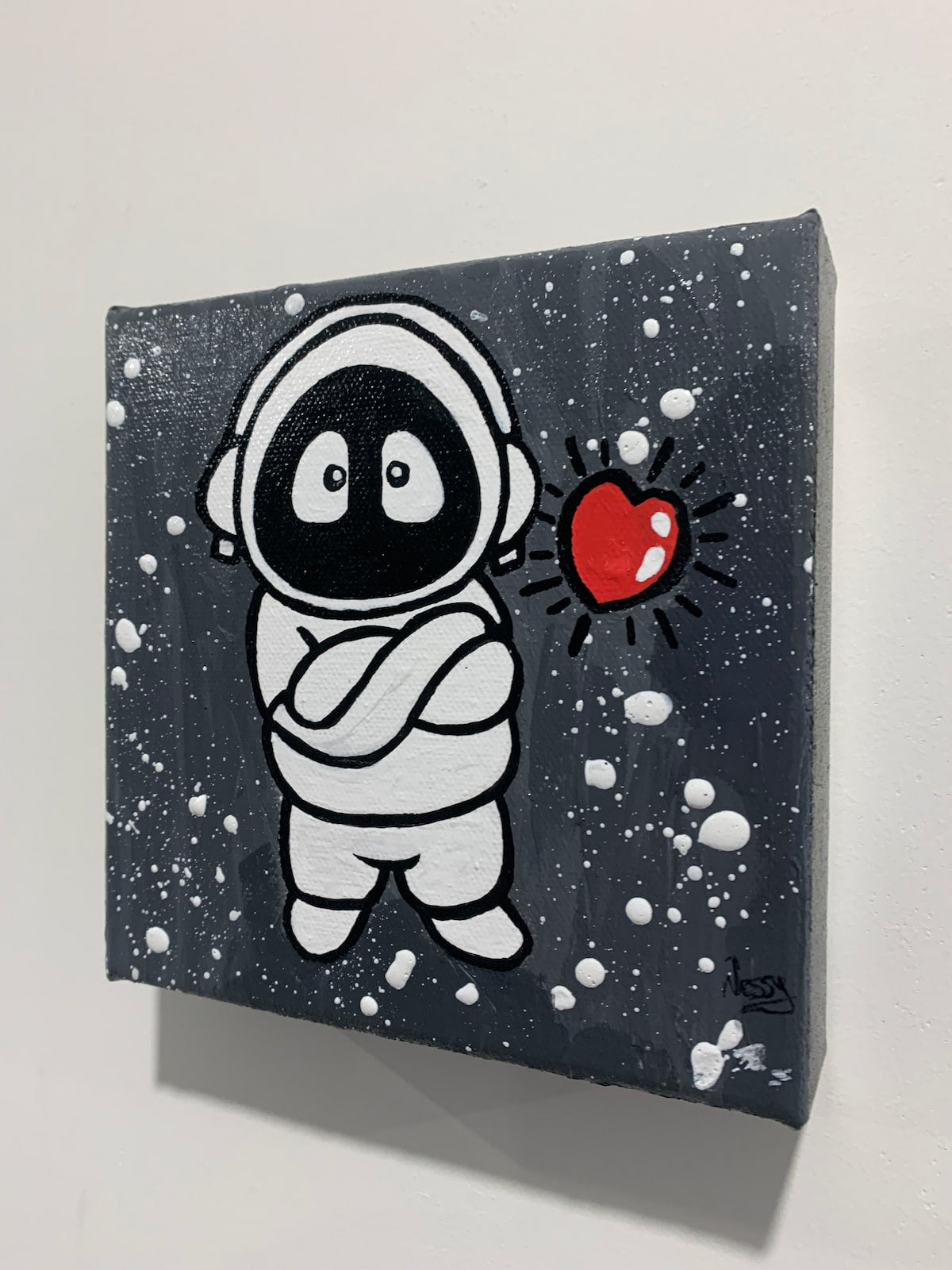 Painting of Hoodie Boy, arms folded, with a floating heart, viewed from the side on a white wall.